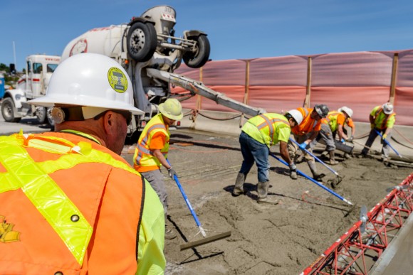 IMCO workers on I-90 bridge Construction workers in hard hats and high visibility vests working on I-90 roadway to place concrete during a closure, with blue sky in background