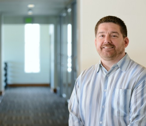 IMCO Director of Finance, Jim Cooper Jim Cooper standing in natural sunlight in office building, wearing striped shirt