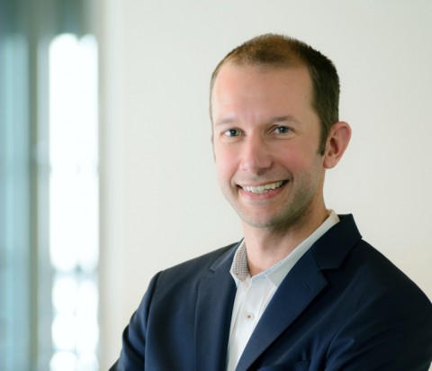 IMCO President Tyler Kimberley portrait Tyler Kimberley, wearing white shirt and navy blazer, standing with arms crossed with natural sunlight